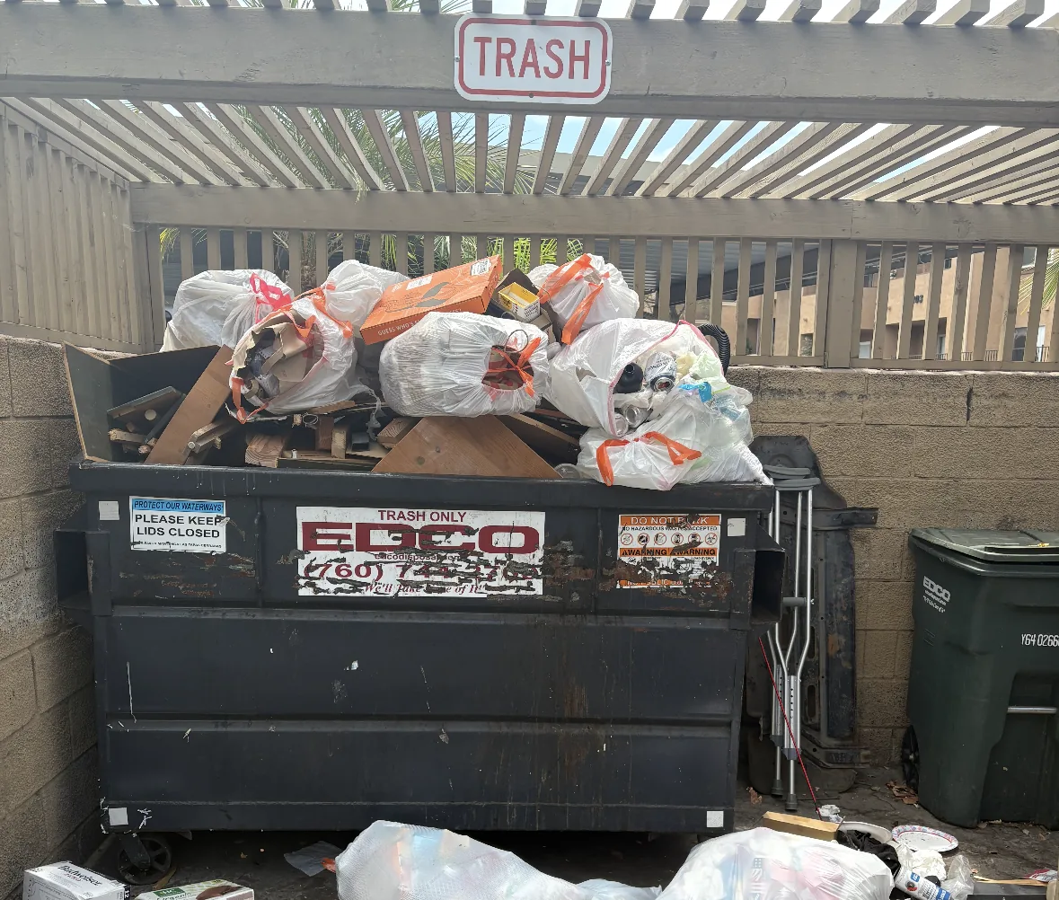 Condo dumpster enclosure with bags and debris piled around the bin
