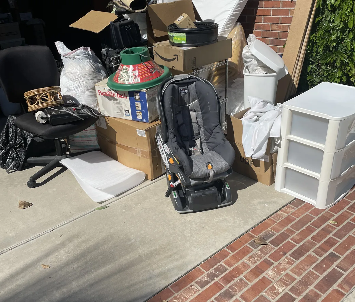 Furniture, boxes, a car seat and bagged household junk piled up in a driveway