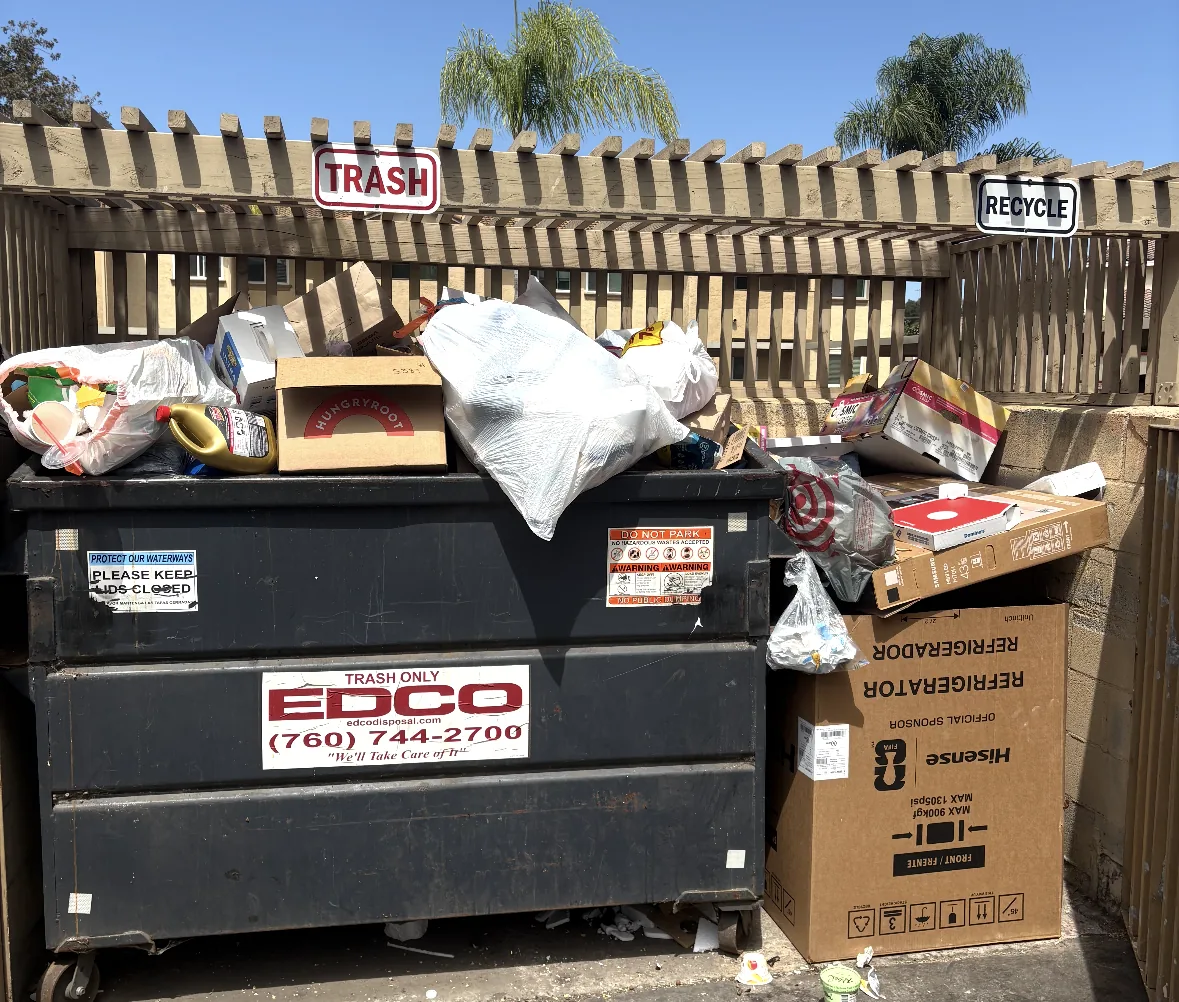 Overflowing dumpster enclosure with boxes and bagged junk at a condo complex