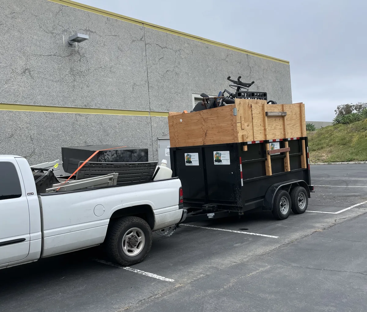 Junk Boyz pickup and loaded dump trailer parked outside a commercial warehouse