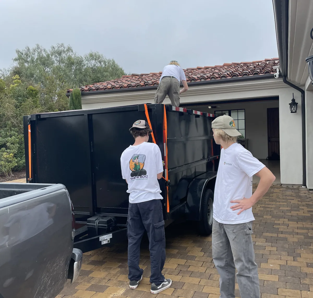 Junk Boyz loading a dump trailer in a driveway, one of the crew up top packing it down