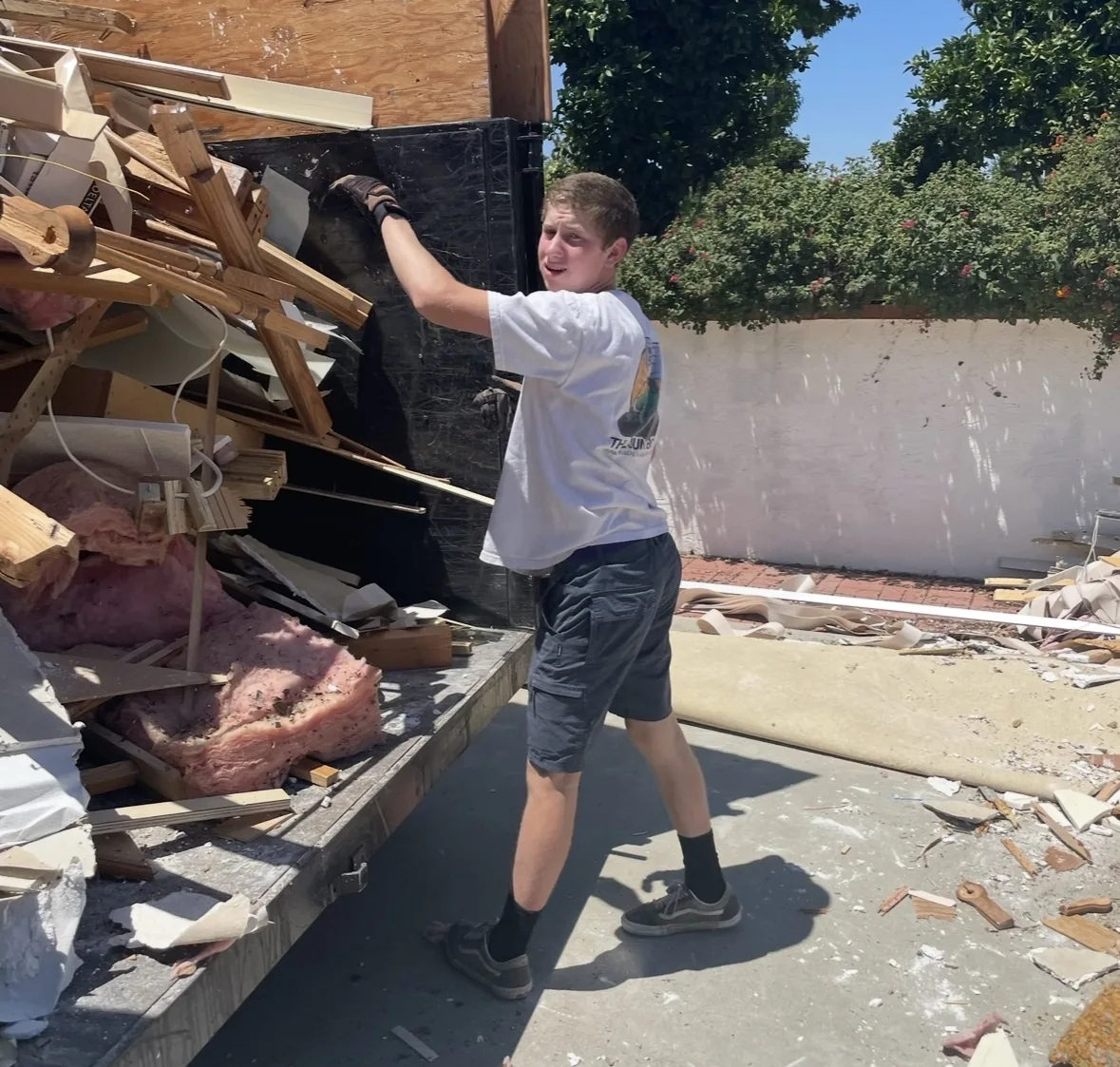 Aidan tossing torn-out wood and drywall into the dump trailer on a demo job